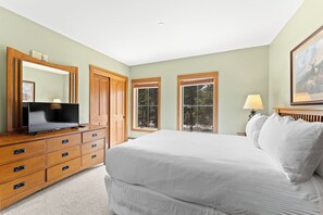 Quarto com cama, cómoda, televisão, janelas e um quadro.