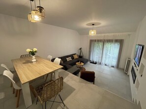 A modern living room with a dining area, a sofa set, a TV, and a large window with curtains. - Charming House - Garden & Near Paris (Cergy)