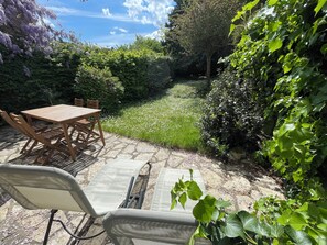 A patio with a table and chairs, surrounded by lush greenery and a stone pathway. - Charming House - Garden & Near Paris (Cergy)