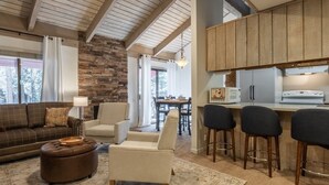 A cozy living room with a stone fireplace, a sofa, a coffee table, and a dining area with a table and chairs. - Sunshine Loft ~ Free Shuttle ~ Pool & Hot Tub (Mammoth Lakes)