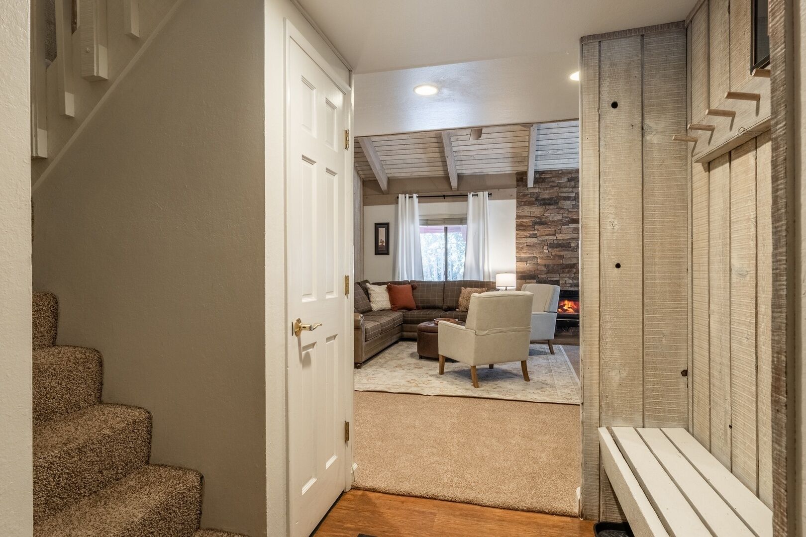 A hallway leading to a living room with a fireplace, a staircase, and a door.