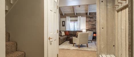 A hallway leading to a living room with a fireplace, a staircase, and a door.