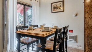 A dining area with a wooden table set for four, chairs, a framed picture on the wall, and a notice about the black heater. - Sunshine Loft ~ Free Shuttle ~ Pool & Hot Tub (Mammoth Lakes)