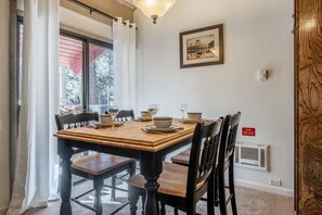Ein Essbereich mit einem Holztisch, gedeckt für vier Personen, Stühlen, einem gerahmten Bild an der Wand und einem Hinweis zum schwarzen Heizgerät.