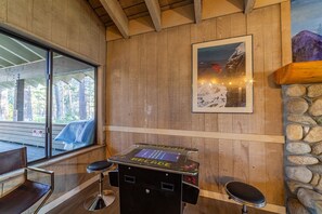 Interior em madeira com mesa de bilhar, banquetas de bar e um quadro com uma montanha nevada.