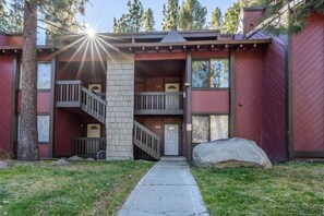 A two-story building with a stone pillar, wooden balconies, and a large rock in the foreground. - Sunshine Loft ~ Free Shuttle ~ Pool & Hot Tub (Mammoth Lakes)
