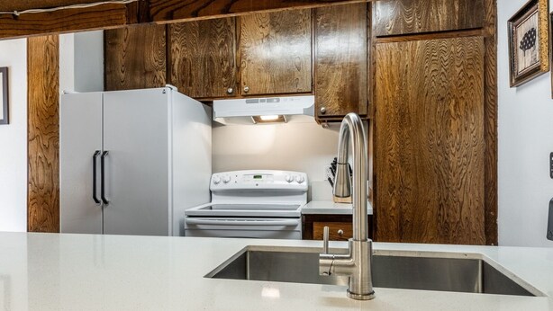 A kitchen with wooden cabinets, a stainless steel sink, and a white stove. - Sunshine Loft ~ Free Shuttle ~ Pool & Hot Tub (Mammoth Lakes)