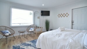 A bedroom with a bed, two wicker chairs, a small table, a TV, and a window with blinds. - SIngle Room - 1 King Bed -Valley View (Himrod)
