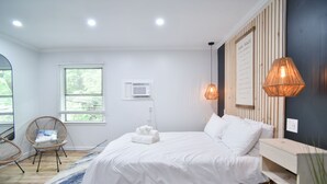 Quarto com cama, cadeira, mesa de cabeceira, luminária, ar-condicionado fixado na parede e janela.
