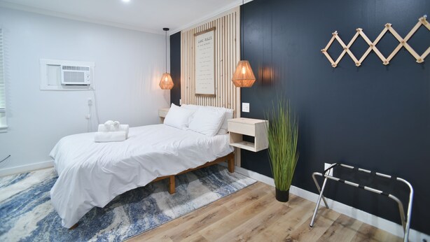 Quarto moderno com cama, mesas de cabeceira, ar condicionado fixado na parede, luminária na parede e um detalhe decorativo.