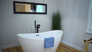 Une salle de bain moderne avec une baignoire sur pieds, un miroir au-dessus et un plancher en bois.