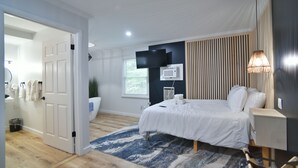 Une chambre à coucher comprenant un lit, une table de chevet, une lampe, un téléviseur, un appareil de climatisation et une porte donnant sur une autre pièce.