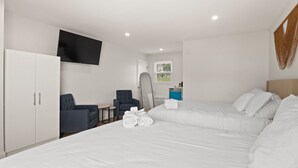 A hotel room with a large bed, a TV mounted on the wall, a chair, a small table, and a window with a view. - Double Room - 2 Queen Beds - Partial Lake View (Himrod)
