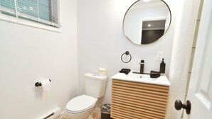 A bathroom with a toilet, a sink, a mirror, and a trash bin. - Double Room - 2 Queen Beds - Pool View (Himrod)