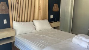 A neatly made bed with white linens, a wooden slat headboard, and a bedside table with a lamp. - Suite - 2 Bedrooms - Pool View (Himrod)