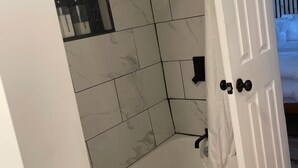 A bathroom with white marble tiles, a black showerhead, and a white door with a handle. - Suite - 2 Bedrooms - Pool View (Himrod)