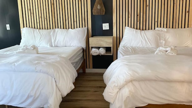 A room with two beds, each with white bedding and pillows, a wooden headboard, and a small wooden nightstand with towels. - Suite - 2 Bedrooms - Pool View (Himrod)