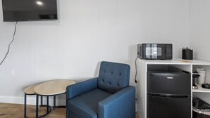 A modern room with a flat-screen TV, a microwave, a black refrigerator, a blue armchair, and a small round table. - Double Room - 2 Queen Beds - Lake View (Himrod)