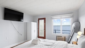 A bedroom with a bed, a TV mounted on the wall, a door, a window with a view of the water, and a bedside lamp. - Single Room - 1 Queen Bed -Valley View (Himrod)