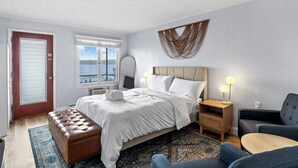 A bedroom with a bed, a bench, a sofa, a nightstand, and a wall-mounted light fixture. - Single Room - 1 Queen Bed -Valley View (Himrod)