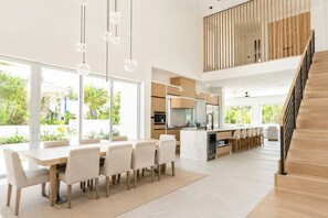 Eine moderne Küche mit einer zentralen Kochinsel, einem Essbereich mit großem Tisch und Stühlen sowie einer Treppe, die in ein Obergeschoss führt.