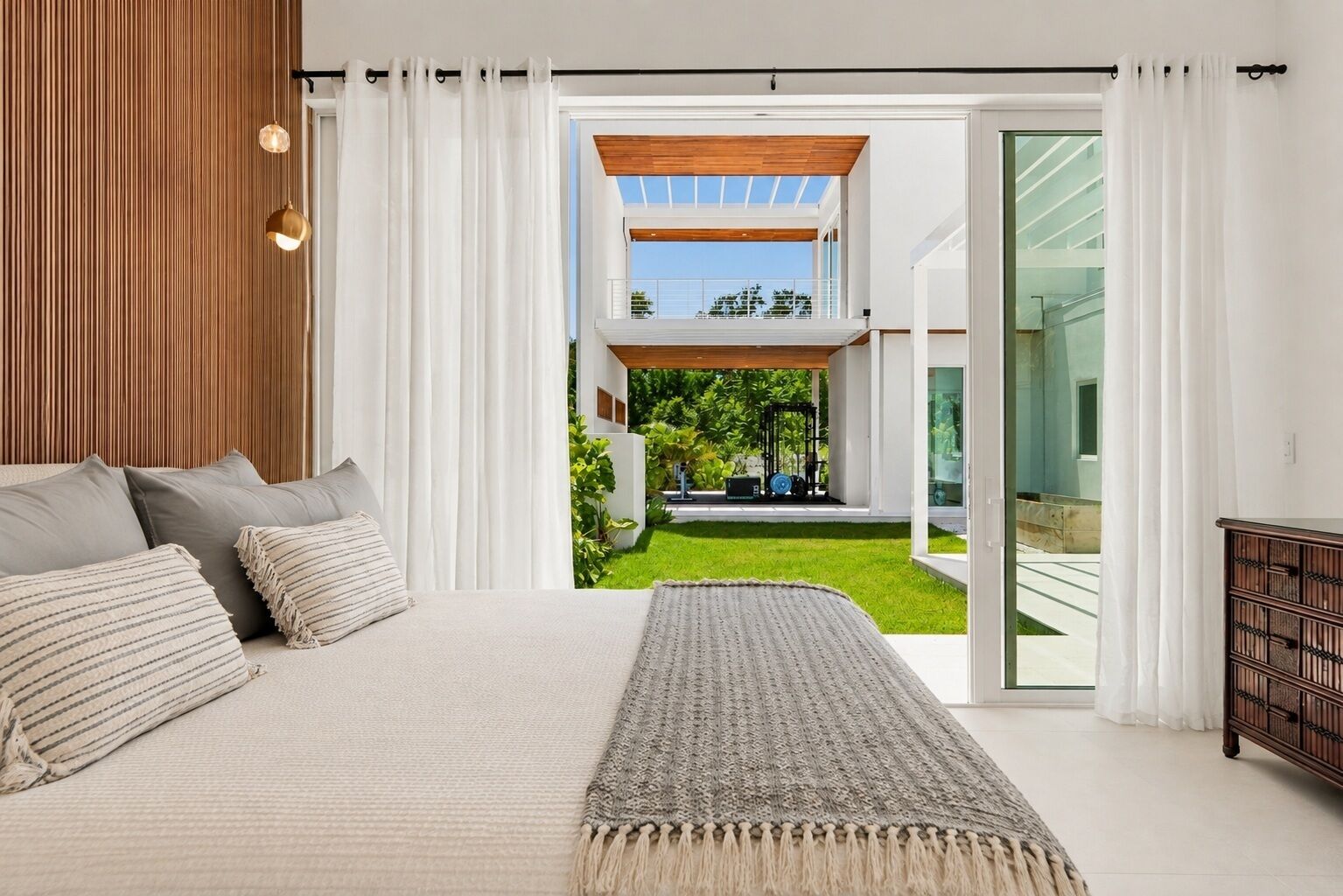 A modern bedroom with a large bed, a view of a garden, and a glass door leading outside.