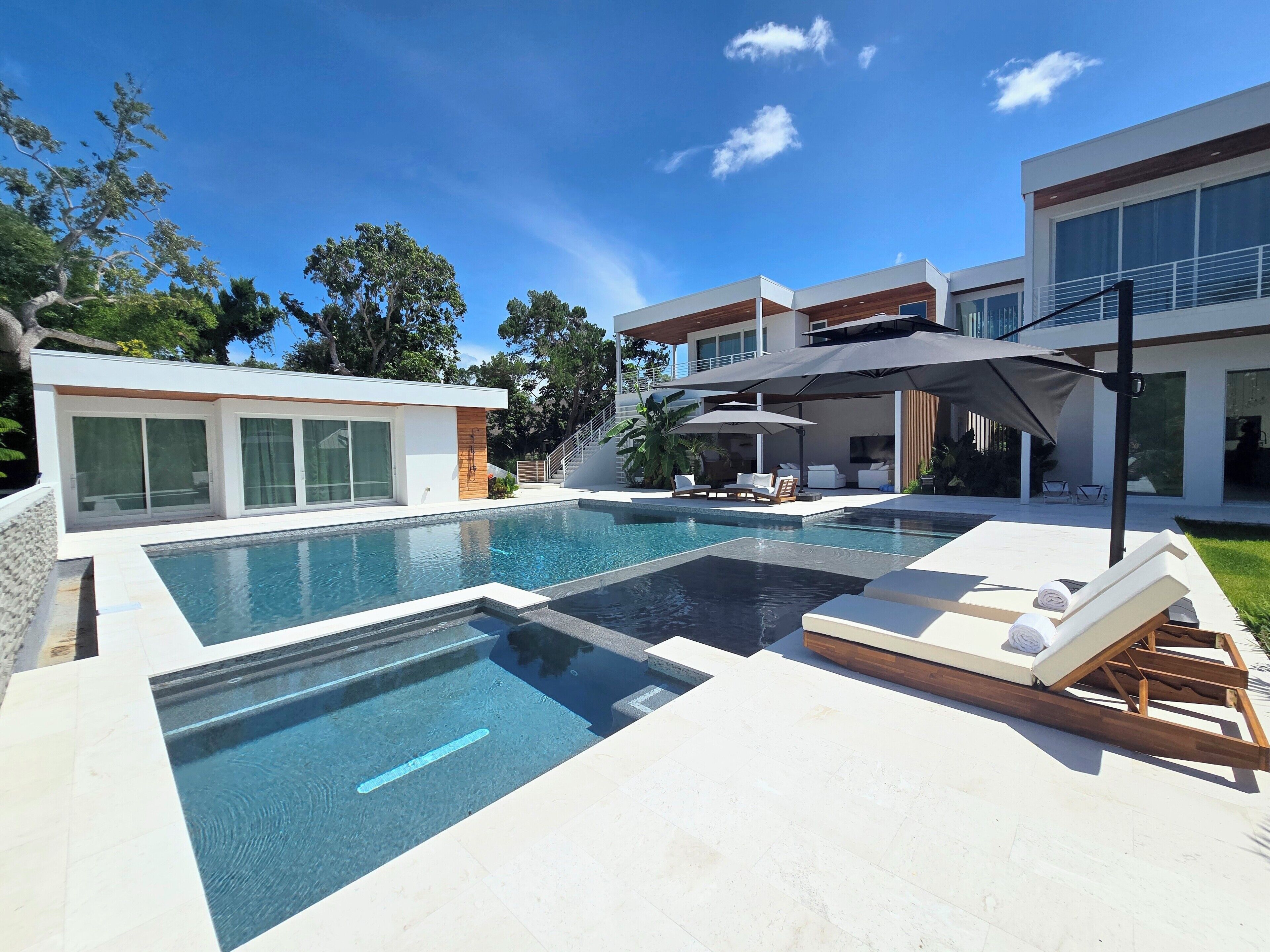 A modern pool area with lounge chairs, a pool, and a two-story house with large windows.