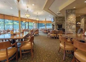 Un vaste espace intérieur aménagé en salle à manger, avec de hauts plafonds, de grandes fenêtres et une cheminée en pierre.
