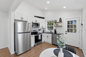 A modern kitchen with stainless steel appliances, white cabinetry, and a dining area with a table and chairs. - Walk to Depot Town - Private Deck & King Bed (Ypsilanti)