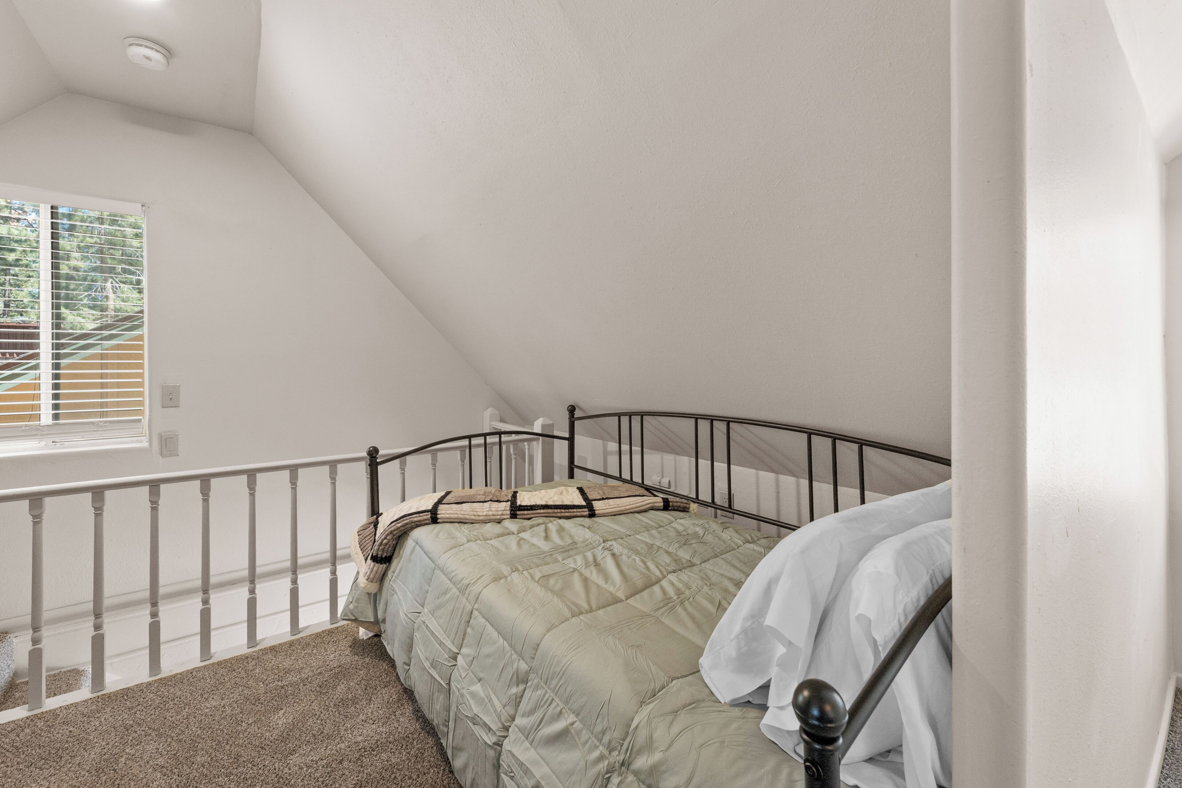 Un dormitorio con una cama, una ventana, una escalera y un techo blanco.
