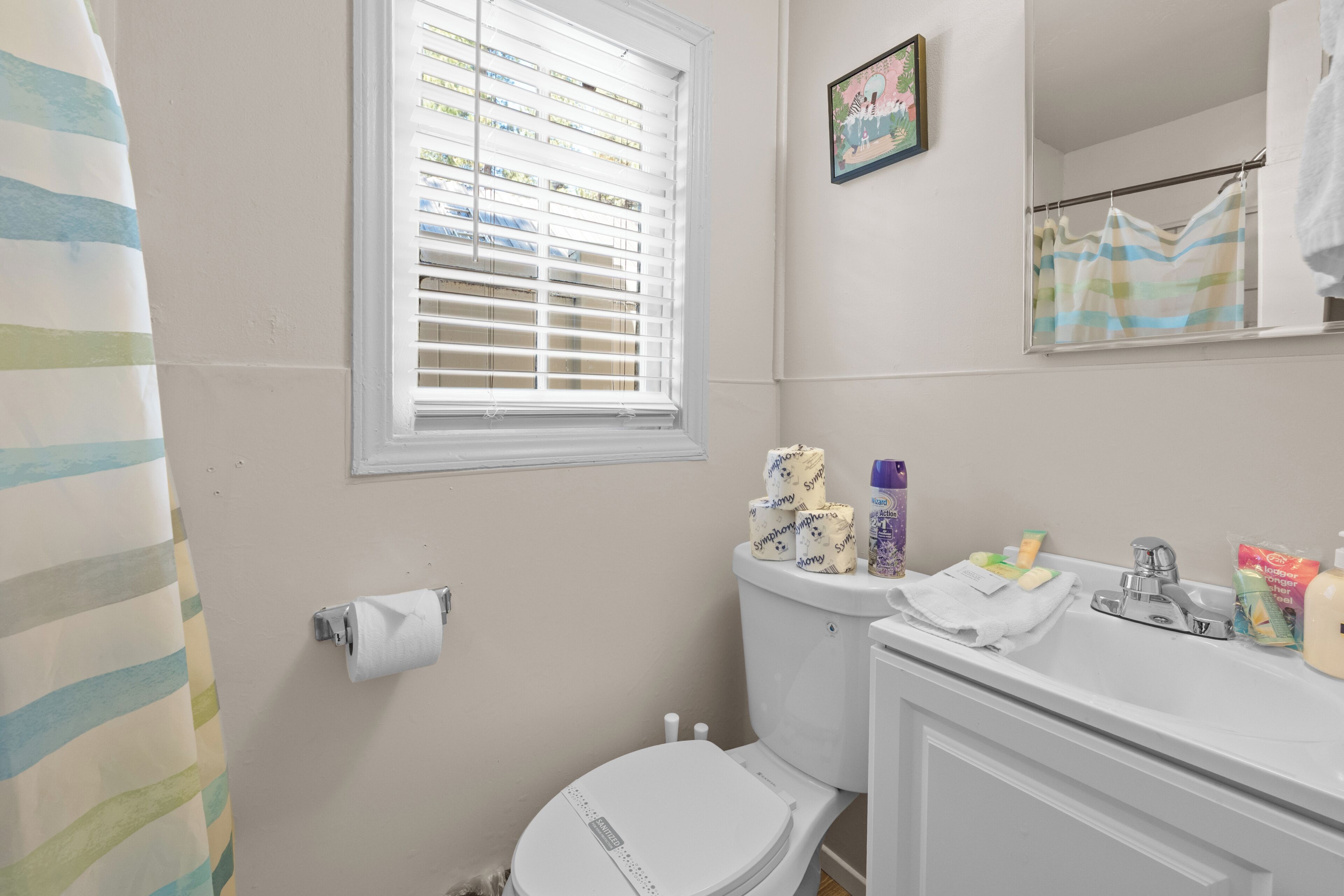 Une salle de bain avec des toilettes, un lavabo et une fenêtre équipée de stores.