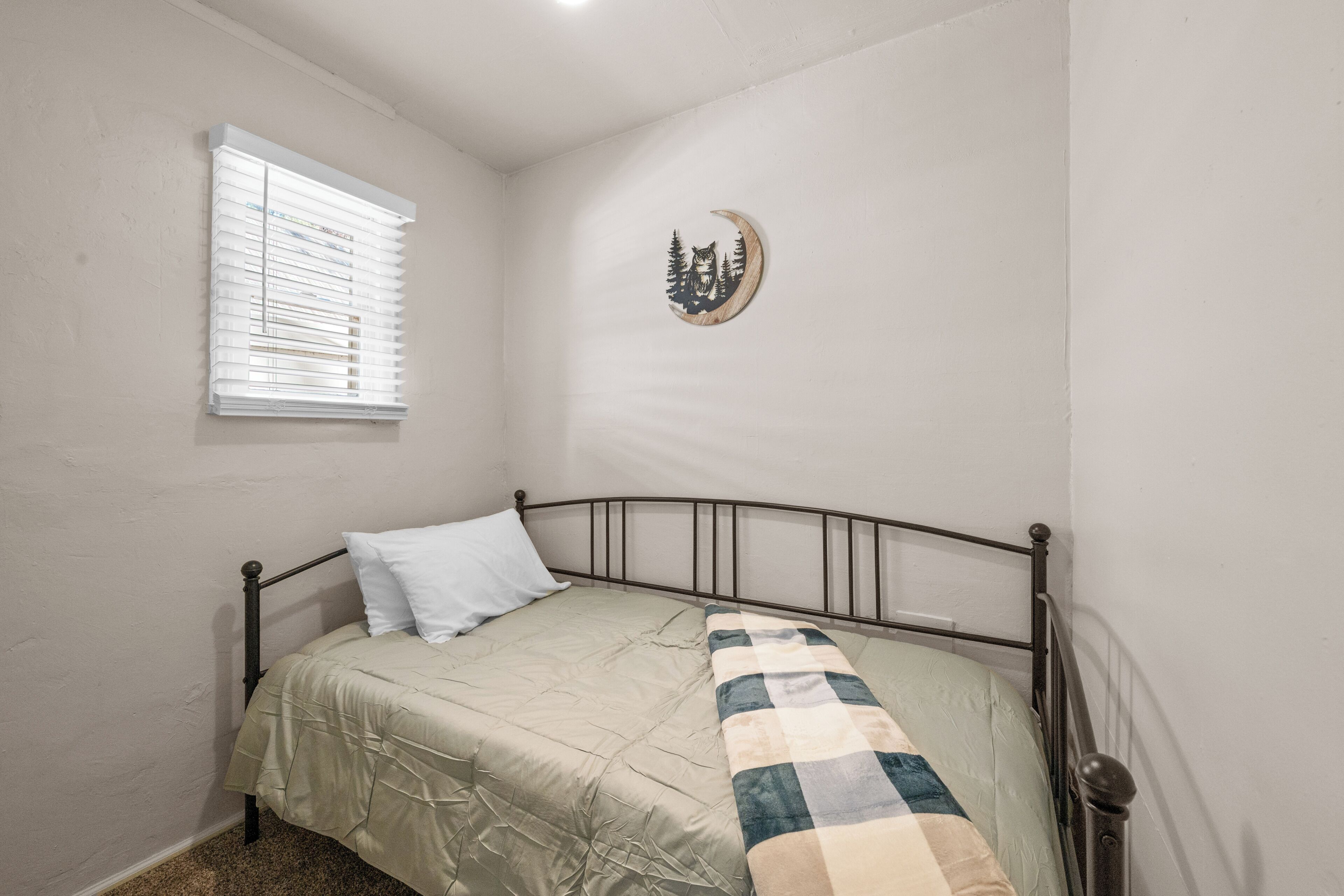 A single bed with a metal frame, a window with blinds, and a wall-mounted decoration.