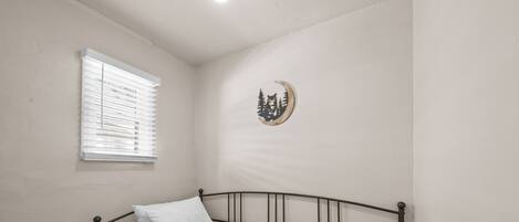 A single bed with a metal frame, a window with blinds, and a wall-mounted decoration.