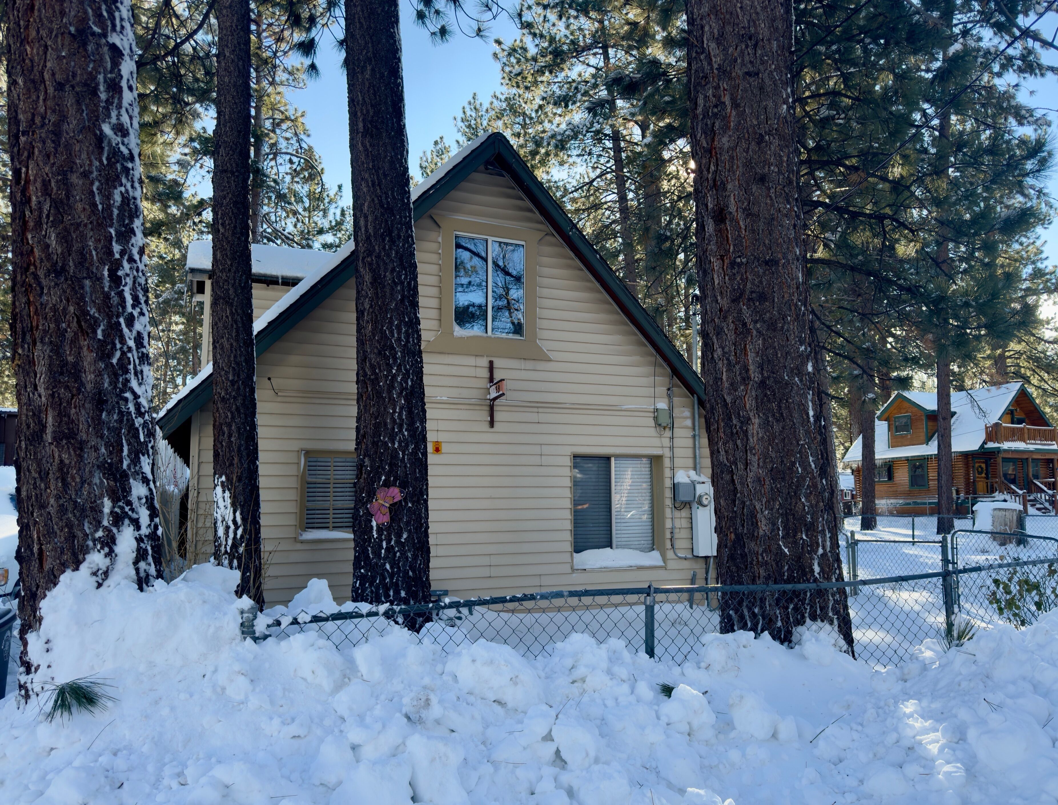Una cabaña de troncos de dos pisos con techo a dos aguas, rodeada de altos pinos cubiertos de nieve.