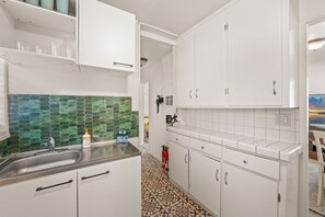 A kitchen with white cabinets, a tiled backsplash, and a sink. - Big Bear 4 Seasons (Big Bear Lake)