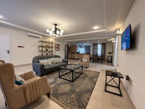 Ein modernes Wohnzimmer mit Sofa, Sessel, Couchtisch und Fernseher.