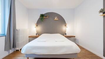 Une chambre à coucher au style minimaliste, avec un lit, des tables de chevet, un radiateur et une fenêtre avec des rideaux.