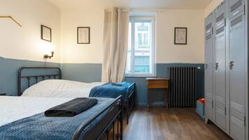 Een slaapzaal met twee bedden, een raam, een radiator en een aantal kasten.