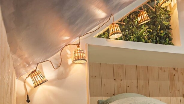 Une chambre mansardée chaleureuse, avec un lit, une petite table et des lampes suspendues.