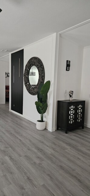 Un intérieur moderne avec un plancher en bois, un grand miroir, une plante en pot et un meuble en bois foncé.