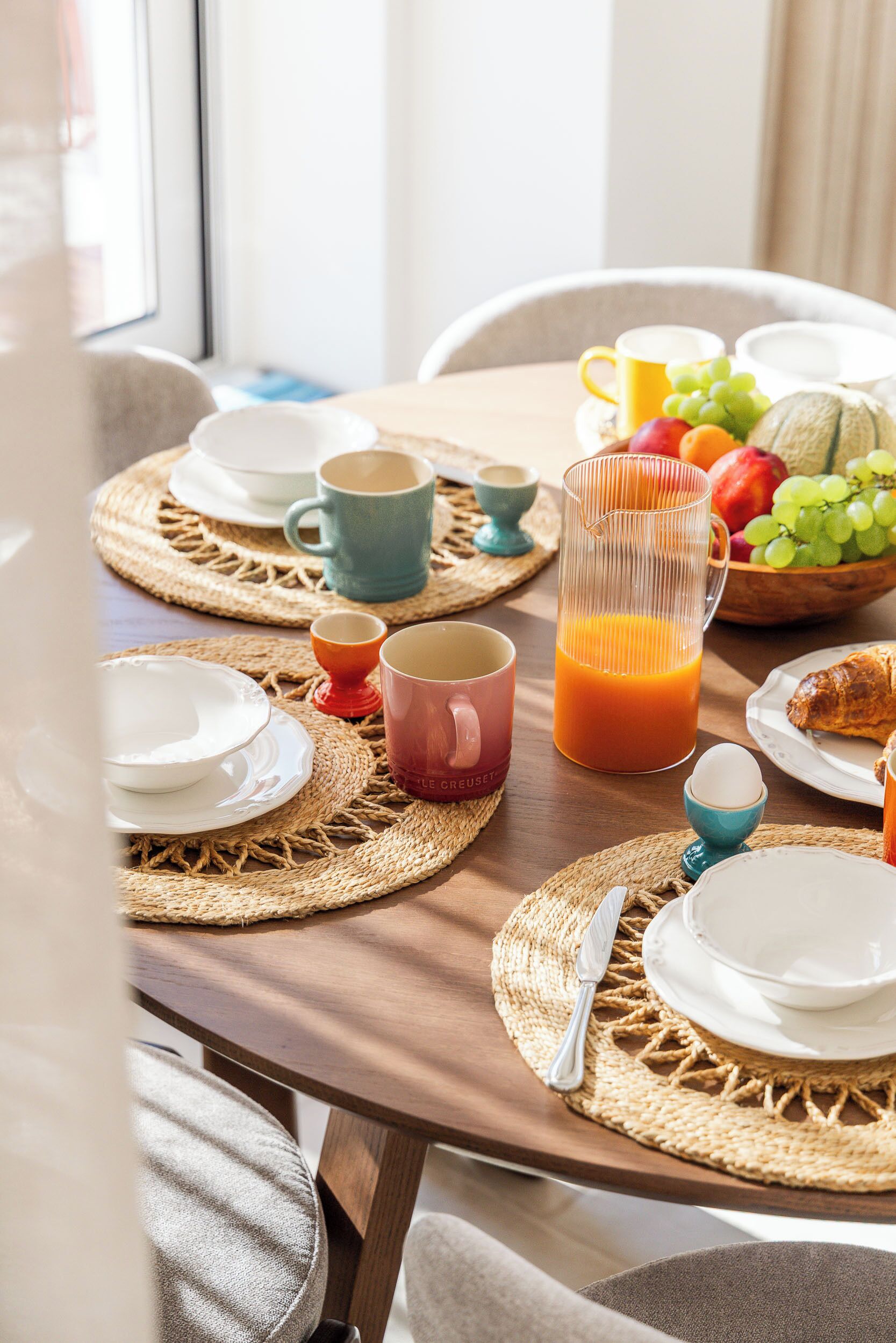 Een ontbijttafel met borden, bekers, een karaf sinaasappelsap en een schaal fruit.