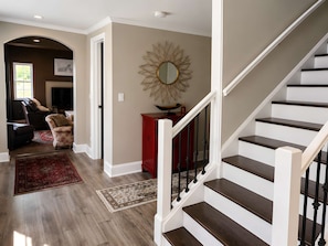 A staircase with wooden steps and a white handrail, leading to a landing with a red cabinet and a decorative mirror. - Spacious Family Retreat w/ Pool, Hot Tub, Fire Pit (Ligonier)