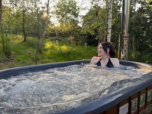 Una persona en un jacuzzi al aire libre rodeada de árboles.