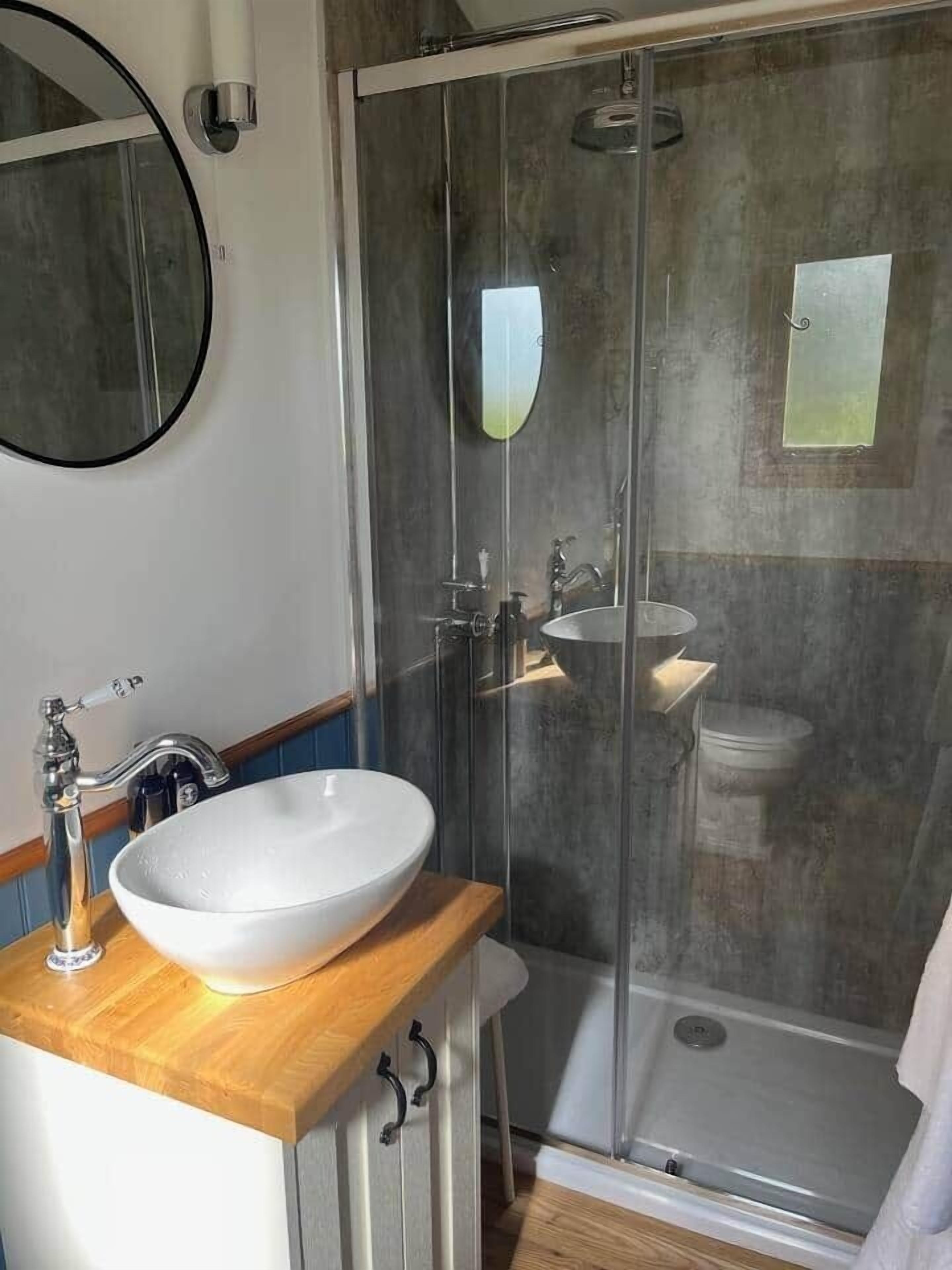Une salle de bain avec un meuble-lavabo en bois, un lavabo blanc, un miroir, un espace douche et des toilettes.