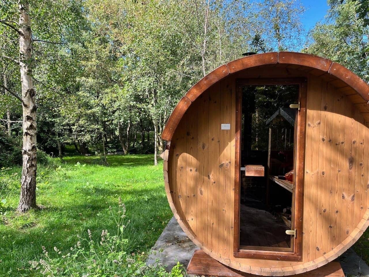 A wooden barrel-shaped structure with a door, surrounded by greenery.