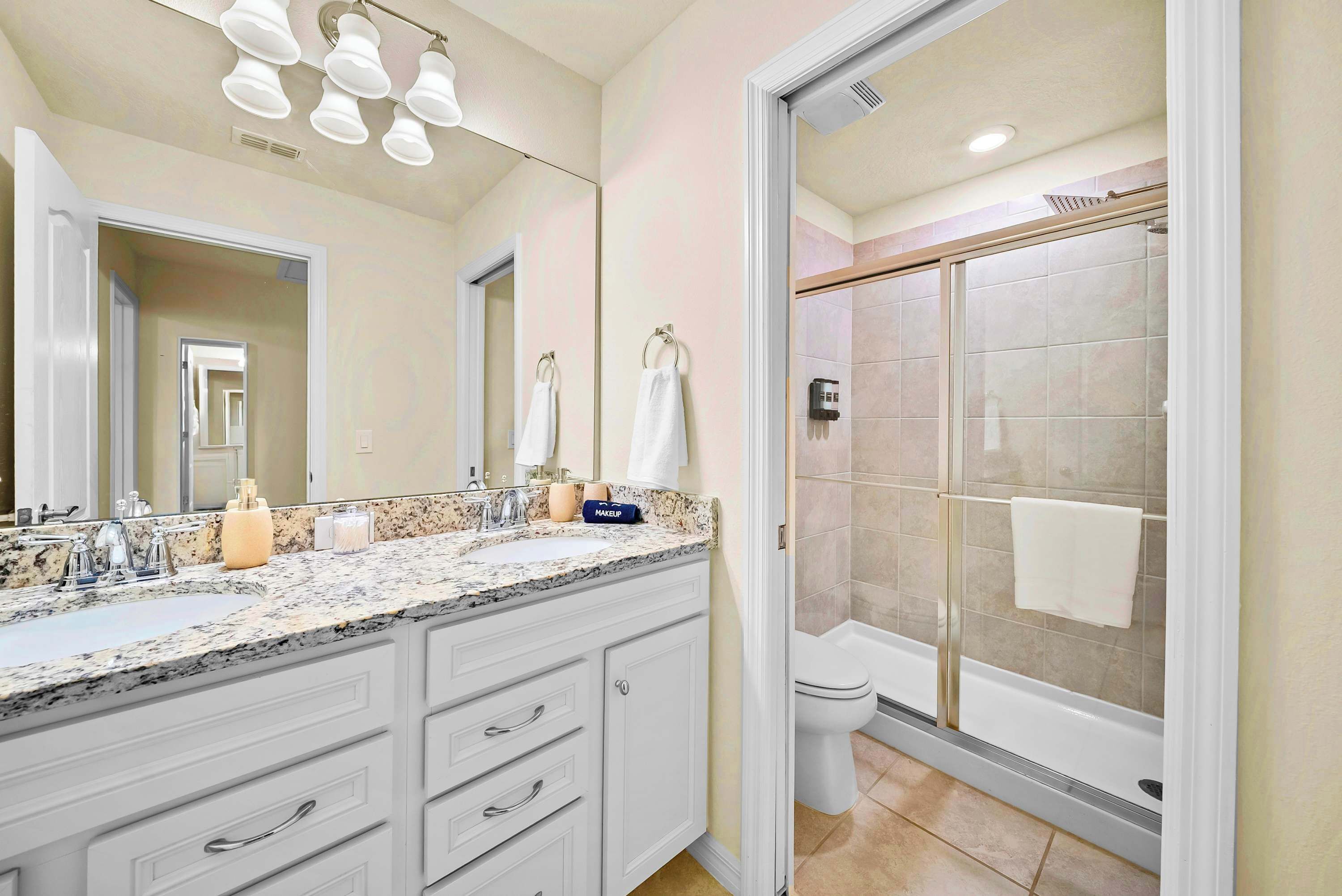 A bathroom with a double sink, a large mirror, a glass-enclosed shower, and a toilet.