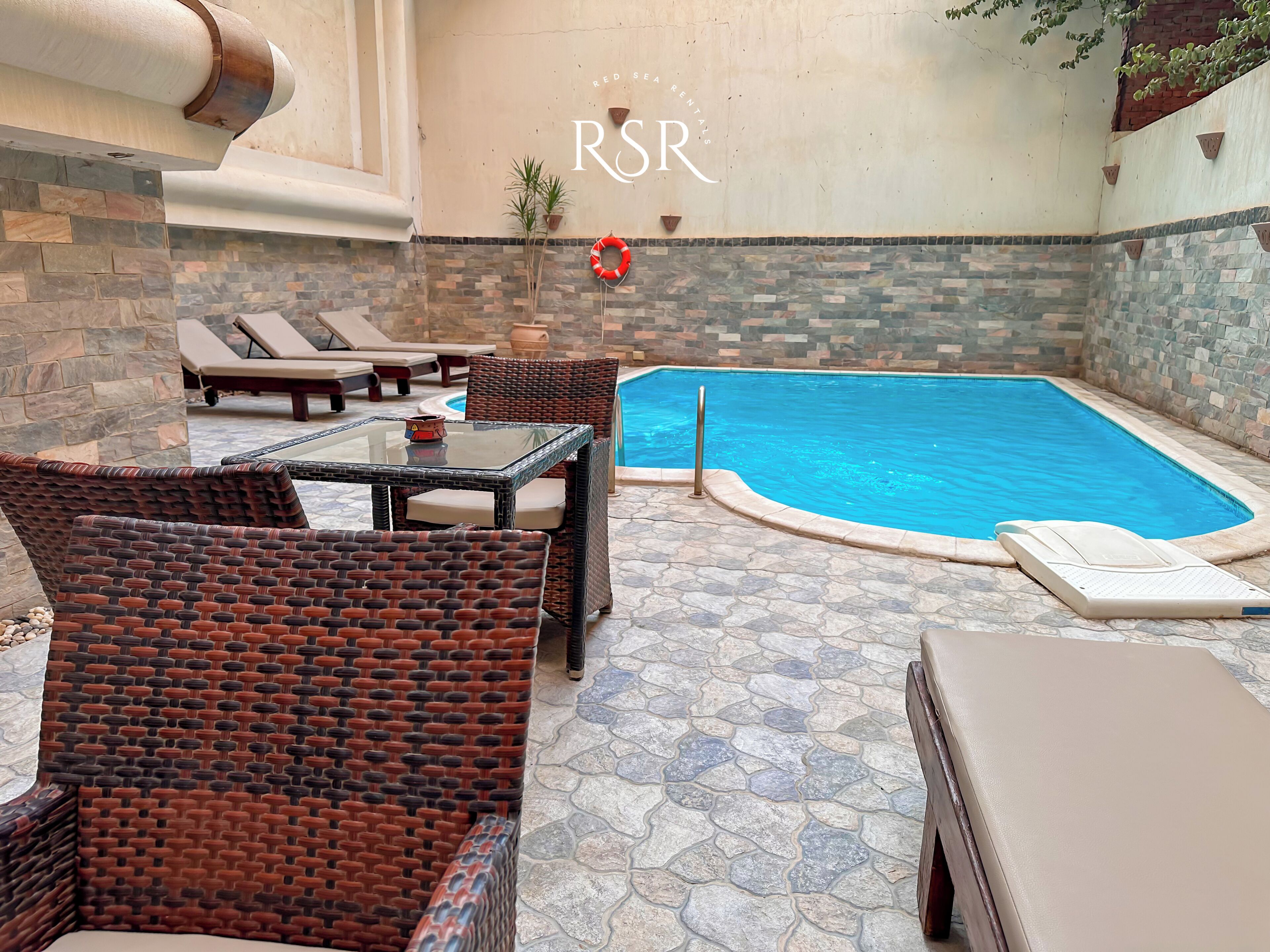 A pool area with wicker furniture, a glass table, and a lifebuoy.