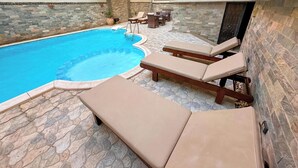Ein Swimmingpool mit Liegestühlen und einer terrasse mit Steinfliesen.
