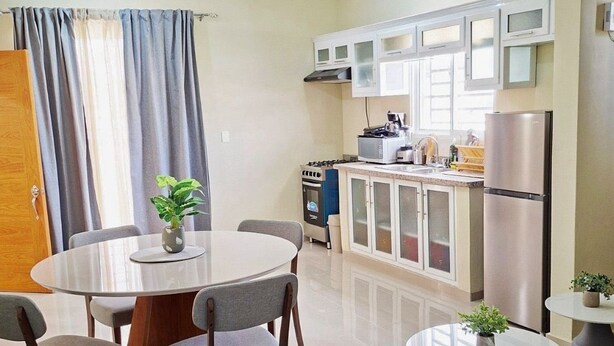 A modern kitchen with white cabinets, a refrigerator, and a stove. There is a dining area with a round table and chairs.