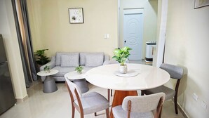 A dining area with a round table, four chairs, a sofa, and two potted plants.